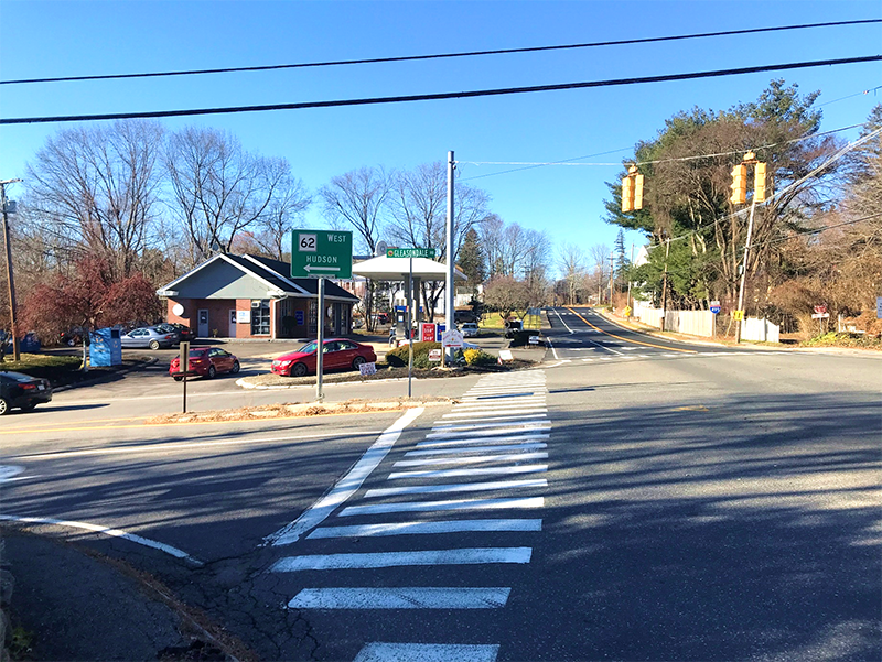 Figure 12 - View across Gleasondale Road (Route 62) of Southwest Intersection Corner. Image shows a long crosswalk that passes to the right of a median and leads to a bed of mulch and vegetation at the perimeter of the gas station parking lot.
